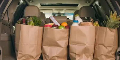 Four brown paper bags filled with food sitting in the trunk of a black SUV.