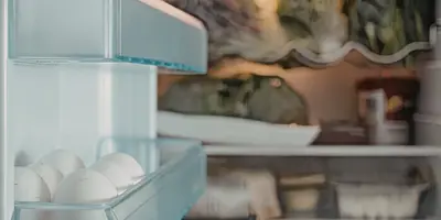 A refrigerator door containing eggs is open, revealing a refrigerator full of out of focus food.