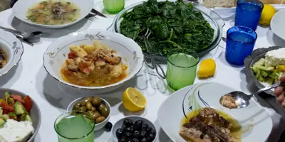 A table full of food and beverages with people eating around it.