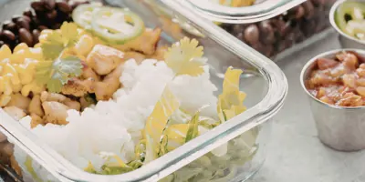Two clear food storage containers filled with rice, beans, and vegetables on top of a gray table.