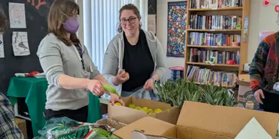 Three people pack boxes full of food for distribution in a food pantry.